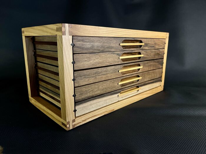 Woodworking project showcasing a handcrafted wooden box with multiple drawers on a black background.