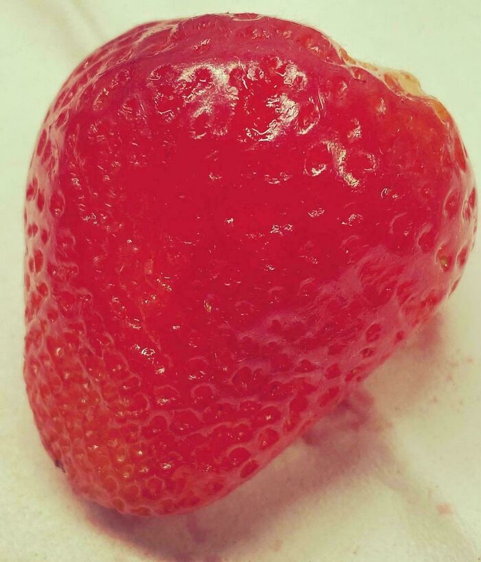 A mildly interesting strawberry shaped like a heart on a white surface.