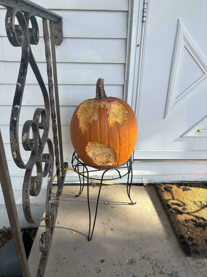 Pumpkin with bite marks arranged to resemble a surprised face, sitting on a stand outside a door, mildly interesting find.