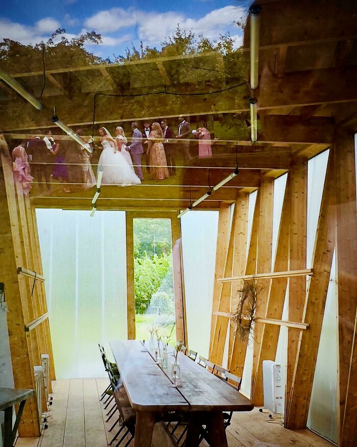 Reflection of people resembling a Renaissance painting, seen on a wooden interior with a long table and chairs.