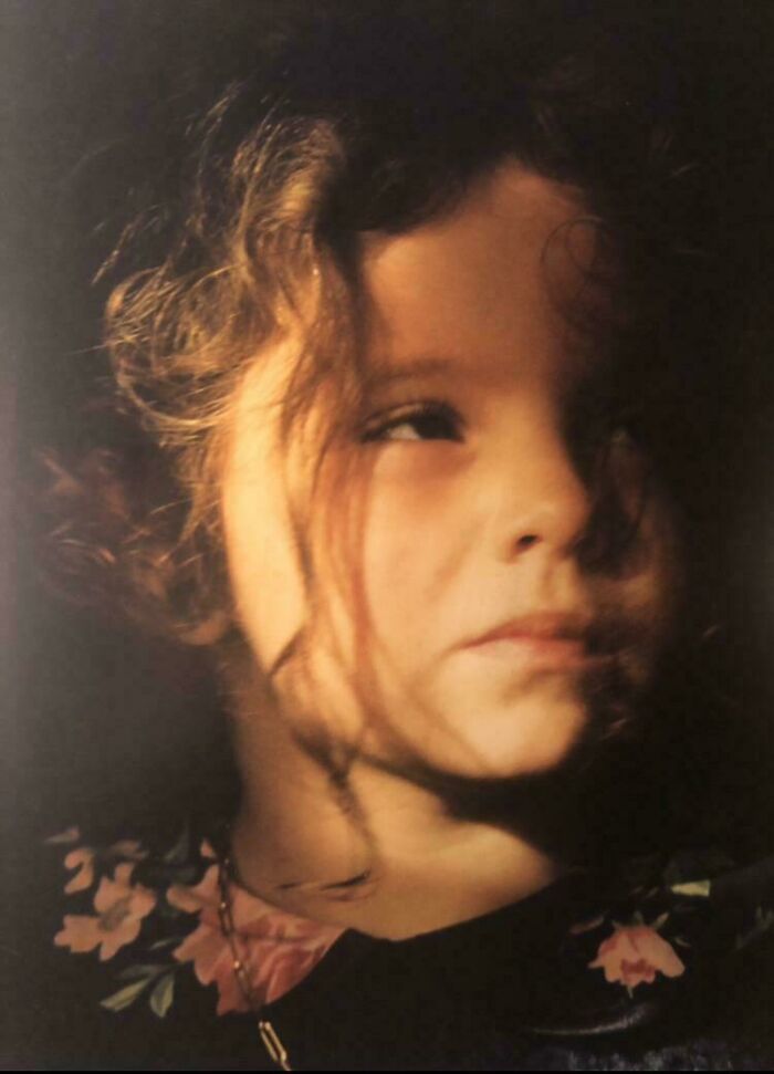 Child in soft light with curly hair, resembling a Renaissance painting.