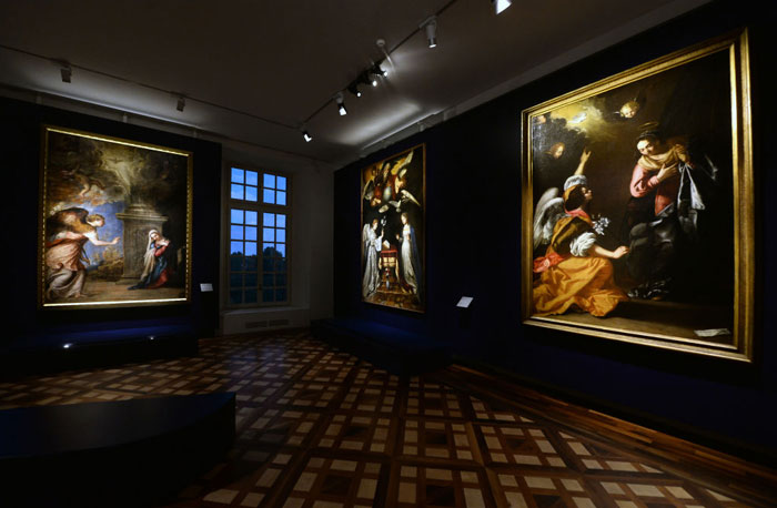 A dimly lit gallery room displaying large Baroque paintings by the famous artist Artemisia Gentileschi , featuring dramatic scenes with rich colors and dynamic lighting.