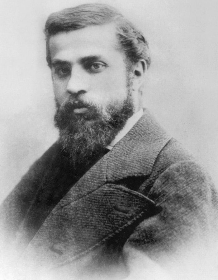 A vintage black-and-white portrait of the famous architect Antoni Gaudí, with a neatly trimmed beard and wearing a suit, looking serious.