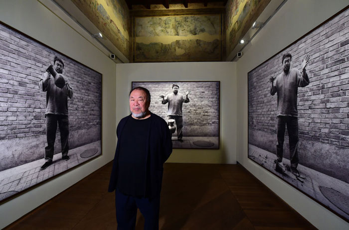  The famous artist Ai Weiwei stands in a gallery surrounded by large black-and-white photographs of himself performing an art action.