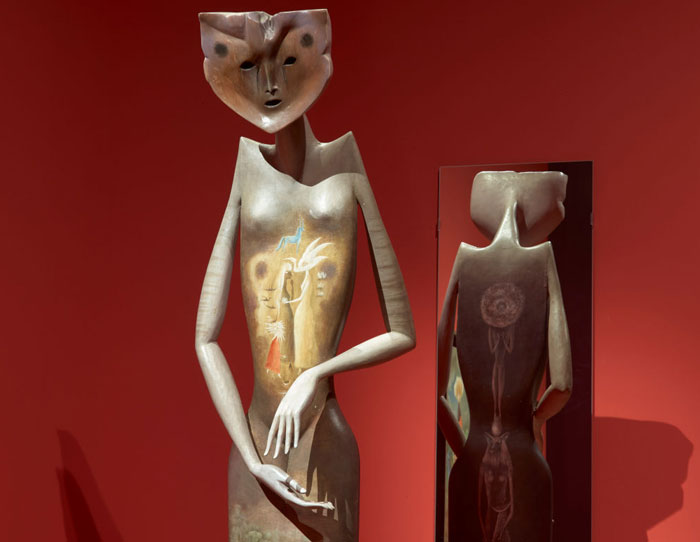 A surreal sculpture by the famous artist Leonora Carrington, featuring a humanoid figure with an elongated body and animal-like head, set against a red background.