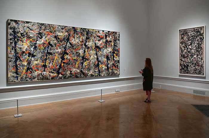 A visitor observes abstract expressionist paintings by the famous artist Jackson Pollock, featuring dynamic splatters of paint on large canvases in a gallery.