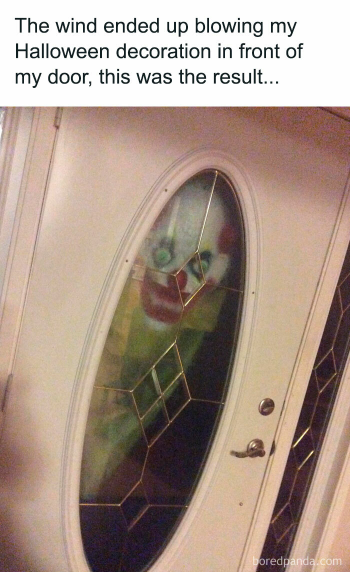 A Halloween meme showing a creepy clown decoration pressed against the glass of a front door. The caption above reads, "The wind ended up blowing my Halloween decoration in front of my door, this was the result..." humorously highlighting the unintentional scary effect.