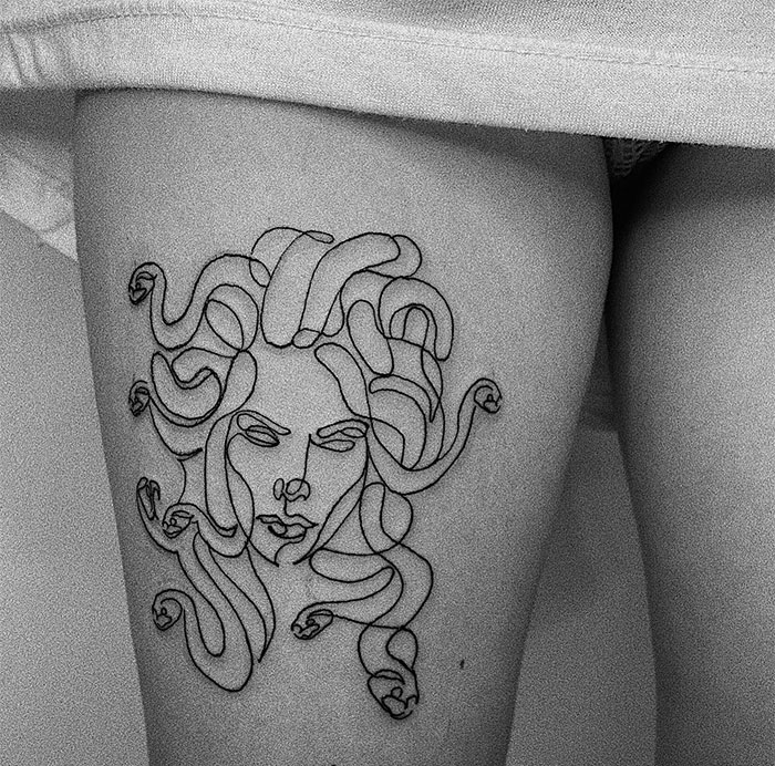 A minimalist Medusa tattoo on the thigh, featuring a single-line style drawing of a woman's face with snakes in her hair, creating a modern and abstract look.