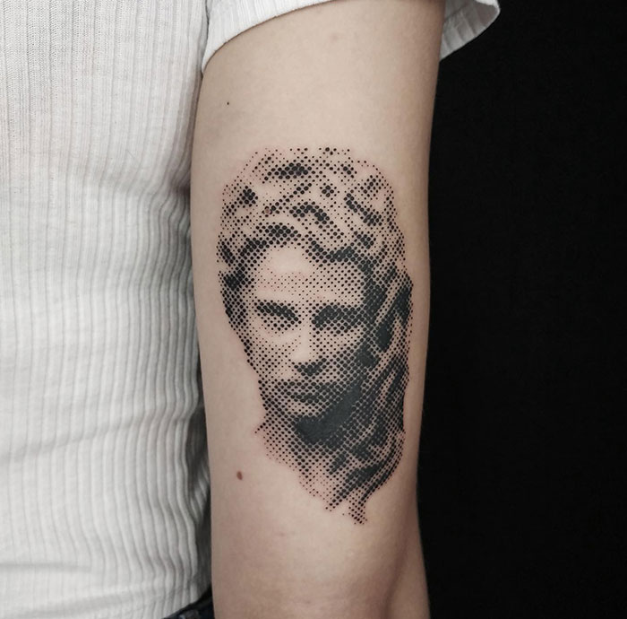  A minimalist Medusa tattoo on the arm, created using a dotwork technique, depicting a face resembling a classical sculpture, with subtle shading and intricate detail.