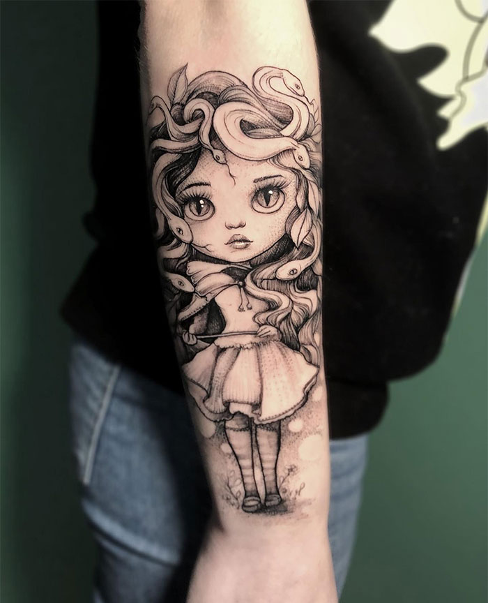  A whimsical Medusa tattoo on the forearm, featuring a doll-like girl with large eyes and snakes entwined in her curly hair, drawn in a playful, cartoonish style.