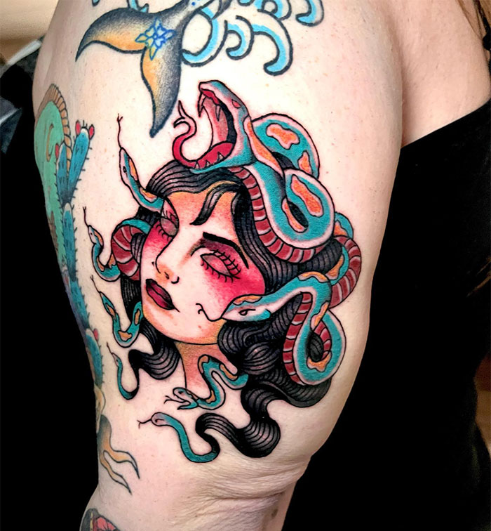 A Medusa tattoo featuring a woman's face with closed eyes and flowing black hair, surrounded by colorful snakes, blending red and blue hues.