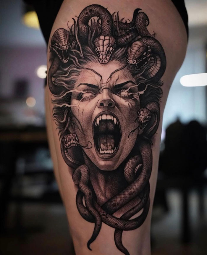 A dramatic black and grey Medusa tattoo featuring a screaming woman's face with fangs, surrounded by snakes in her hair, creating a fierce and intense expression.