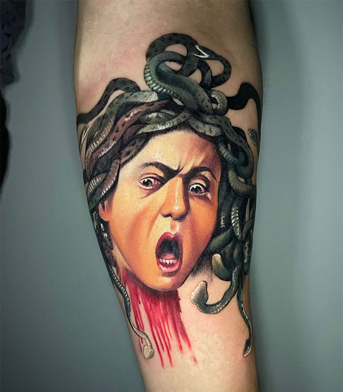 A colorful Medusa tattoo featuring a shocked expression, with snakes in her hair and a blood-dripping neck, capturing a bold and intense design on the arm.