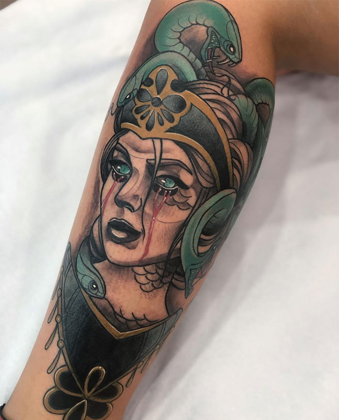 A colorful Medusa tattoo featuring a woman's face with green snakes coiling around her head, tears of blood running down her cheeks, and intricate details on her armor and headpiece.