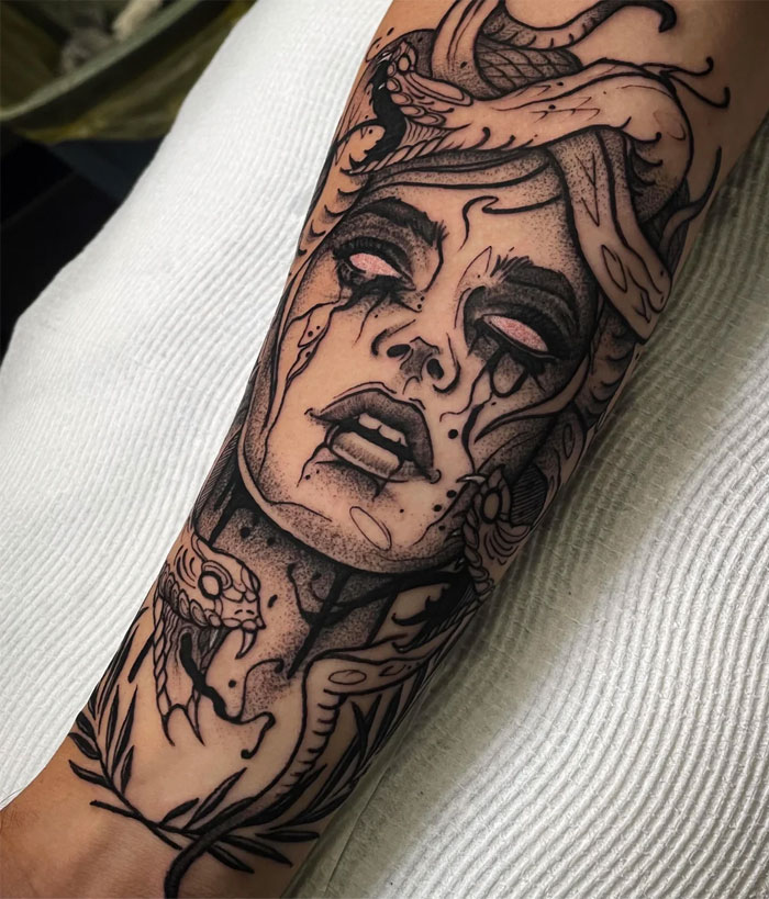 A dark and dramatic Medusa tattoo on the forearm, featuring a woman's face with snakes in her hair, intense shading, and tears streaming from her eyes.