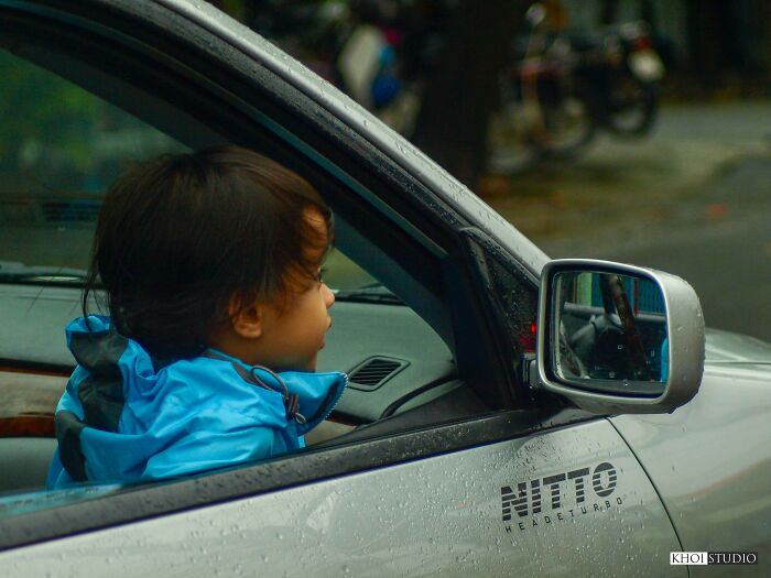 A Child Watches The Street In Gloomy Weather, From Inside A Car