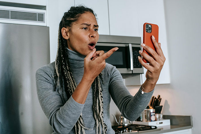 Woman reacting to a phone call in a kitchen, discussing tipping habits.