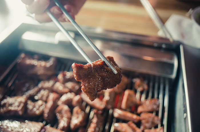 Grilled meat being picked up with chopsticks, symbolizing dining out and tipping practices.