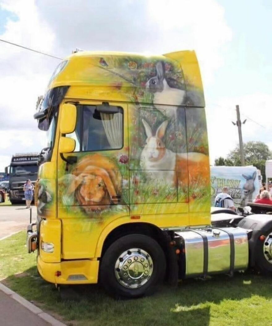 Yellow truck with funny cute images of rabbits painted on the side, parked at an outdoor event.