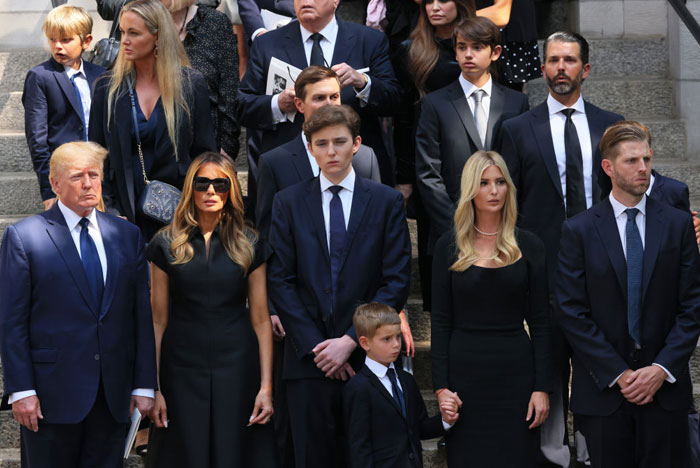 Barron Trump stands in the center of a formal family gathering, his height towering over others, accentuating Barron Trump's height in the group.