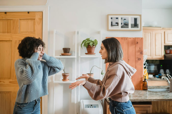 Two women arguing in a kitchen, one looks frustrated while the other explains her point.