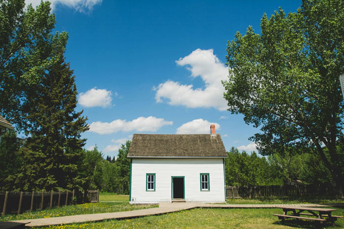 A small white house with a wooden roof surrounded by trees, under a clear blue sky.