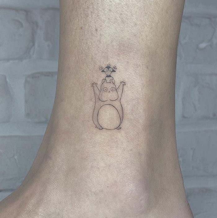 A small tattoo of a minimalistic Totoro with a tiny creature standing on its head.