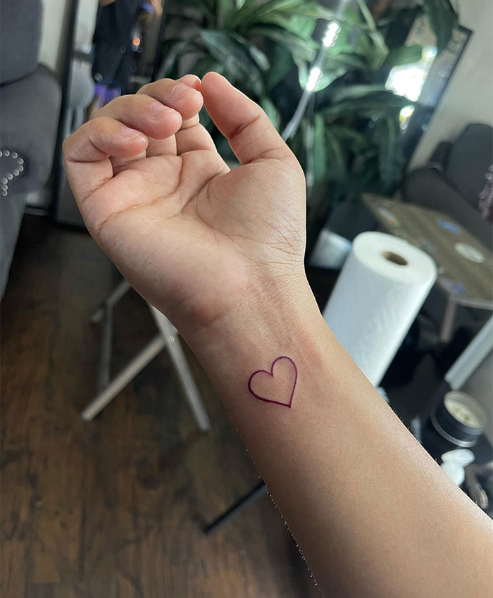  "A small tattoo idea of a simple outlined heart in purple ink on the inner wrist, showcasing a minimalistic and elegant design."