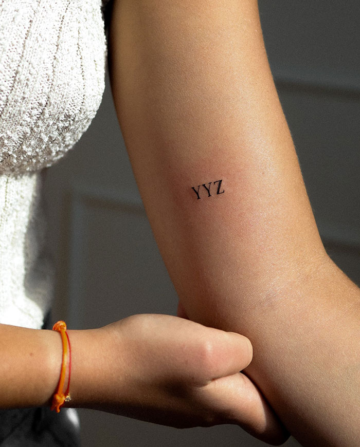 "A small tattoo idea featuring the text 'YYZ' in black ink on the inner arm, adding a minimalist and personal touch."