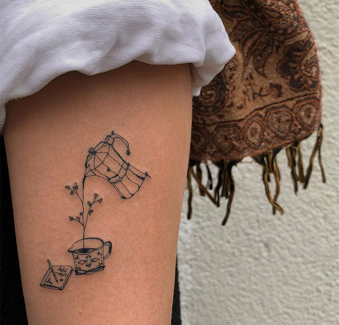 "A small tattoo idea featuring a whimsical scene with a hand pouring a plant into a cup, accompanied by a small book, creating a cozy aesthetic."