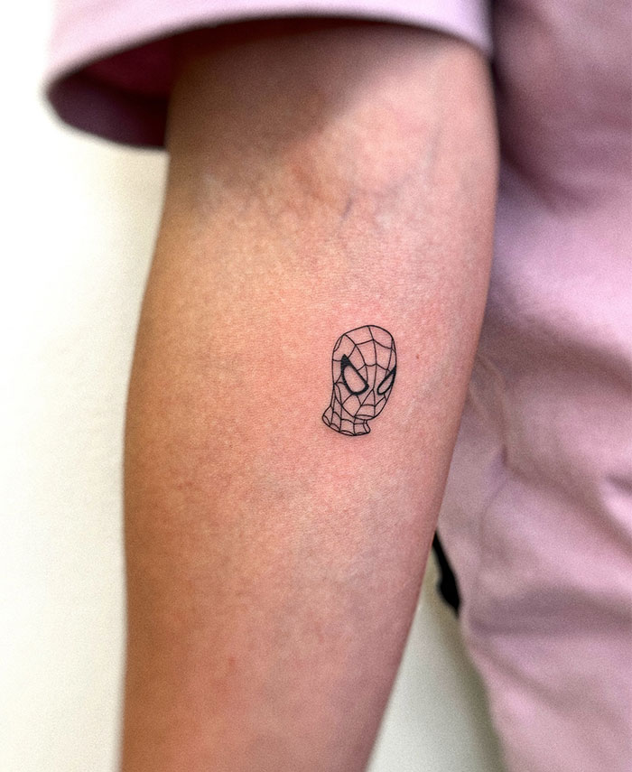 "A small tattoo idea featuring a minimalist outline of a superhero mask with web details on the forearm, adding a subtle comic-inspired touch."