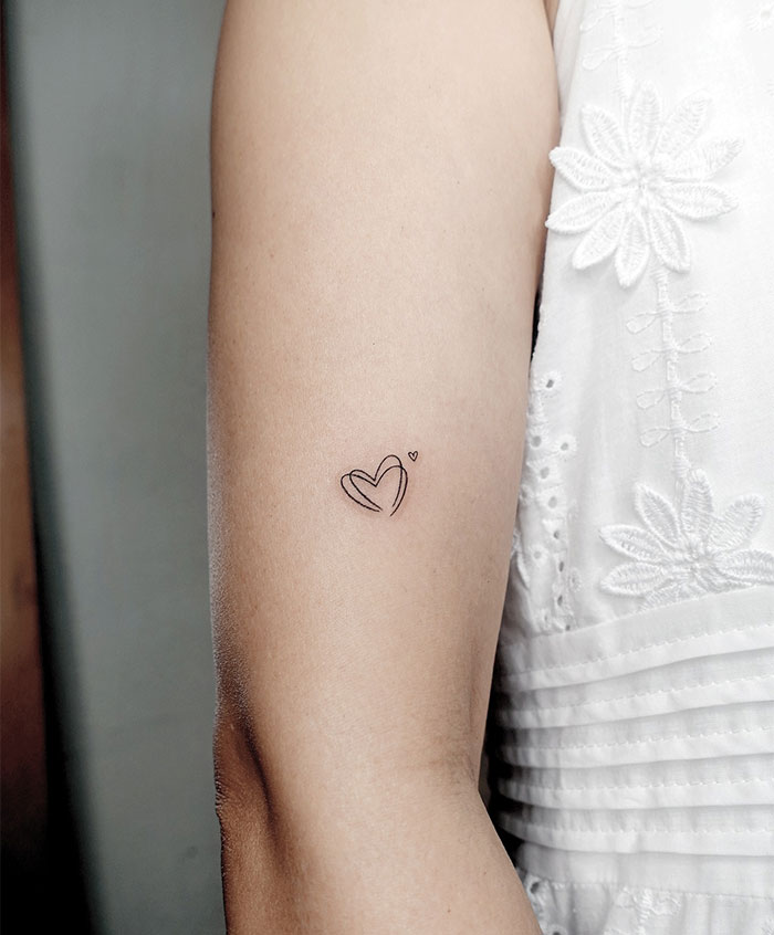 "A small tattoo idea featuring two overlapping heart outlines with a tiny heart above them on the upper arm, adding a delicate and romantic touch."