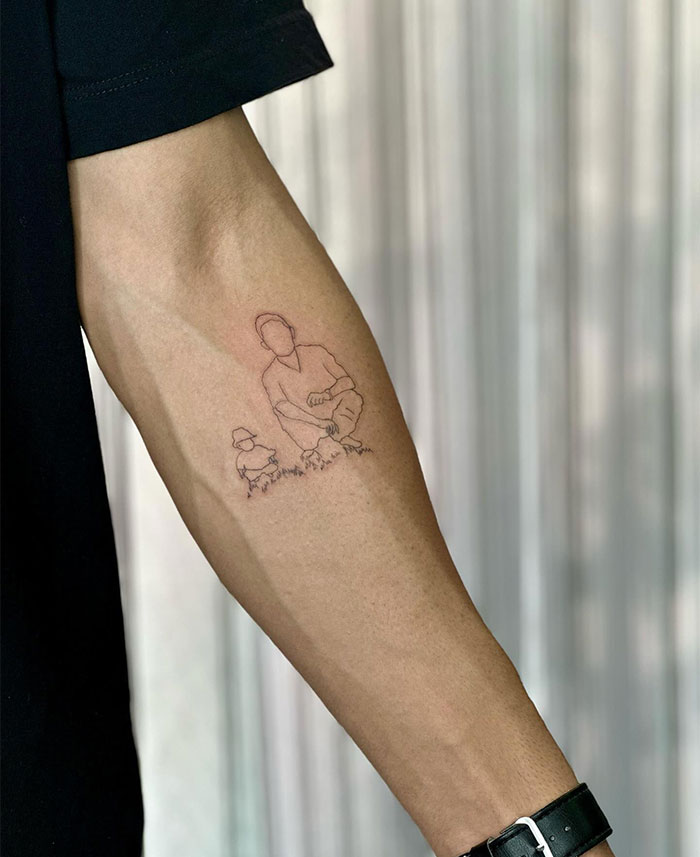 "A small tattoo idea featuring a minimalistic line drawing of a person squatting beside a child and a dog, capturing a sentimental moment on the forearm."