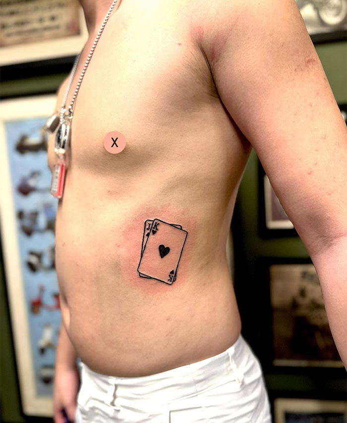  "A small tattoo idea of a playing card with a heart symbol on the side of the torso, creating a bold and stylish design."