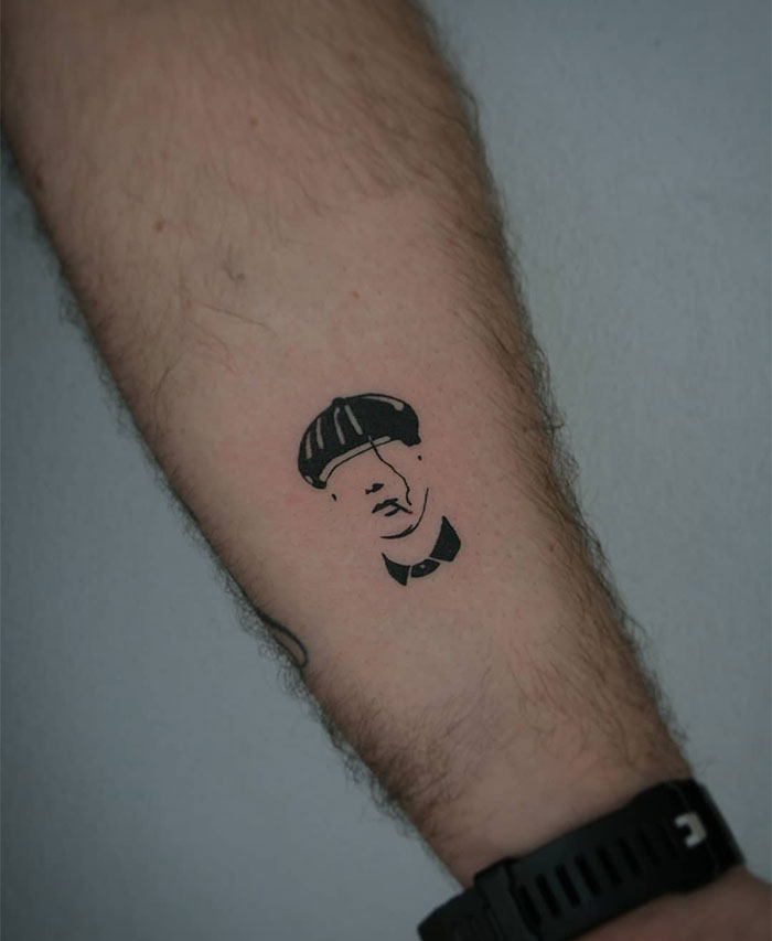 "A small tattoo idea featuring a minimalist, stylized portrait of a person wearing a hat on the forearm, creating a subtle and artistic design."