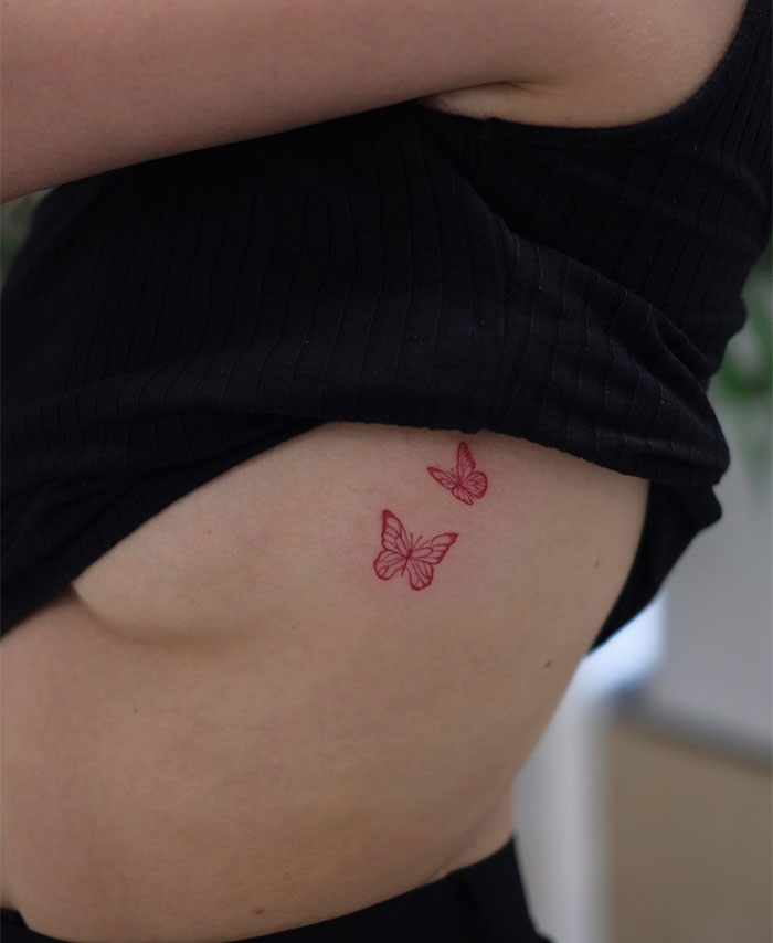 "A small tattoo idea featuring two delicate red butterflies on the side of the torso, adding a vibrant and feminine touch."