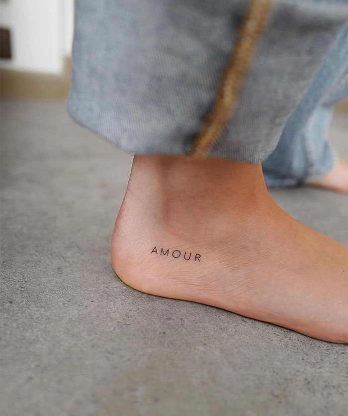 "A small tattoo idea featuring the word 'AMOUR' in a minimalist font on the side of the foot, symbolizing love with subtle elegance."