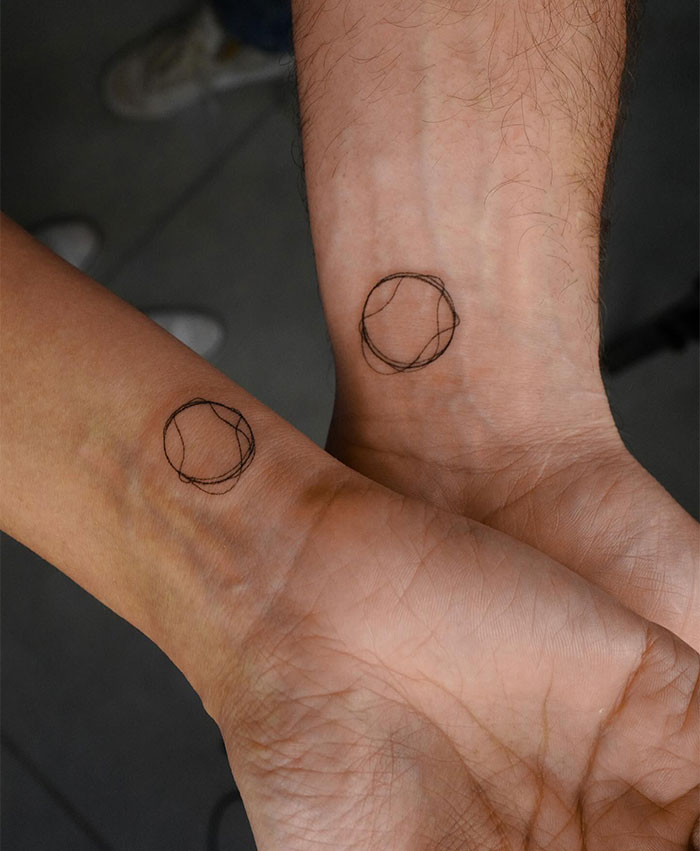 "A small tattoo idea for couples with minimalist overlapping circle designs on each wrist, symbolizing unity and connection."