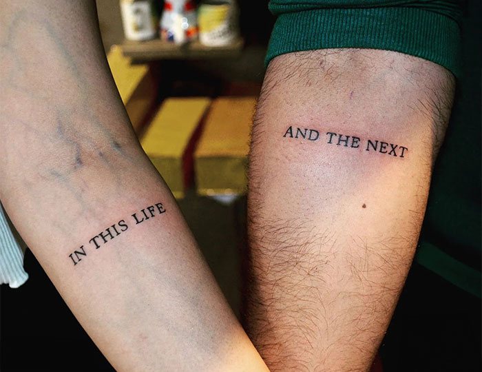 "A meaningful small tattoo idea for couples with complementary text tattoos reading 'In this life' on one arm and 'And the next' on the other."