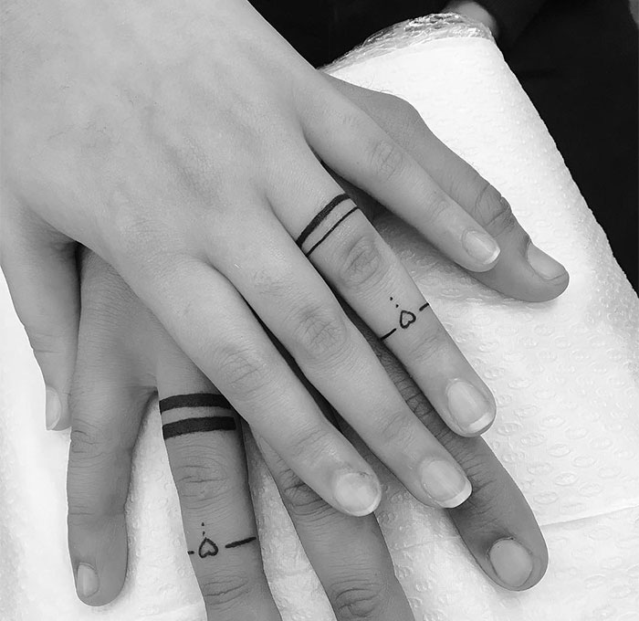 "A small tattoo idea for couples, featuring matching ring finger tattoos with lines and small heart designs, symbolizing unity and connection."