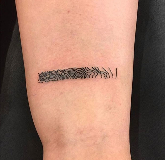 A small tattoo idea featuring a minimalist topographic line pattern within a narrow rectangle on the upper leg.