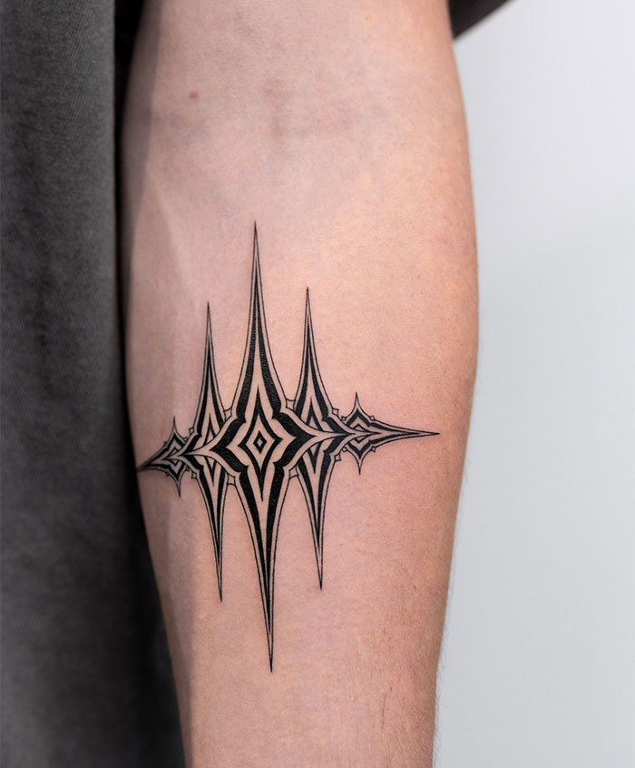 A small tattoo idea featuring an intricate symmetrical design with sharp, spiked edges and layered geometric shapes, inked on the forearm.