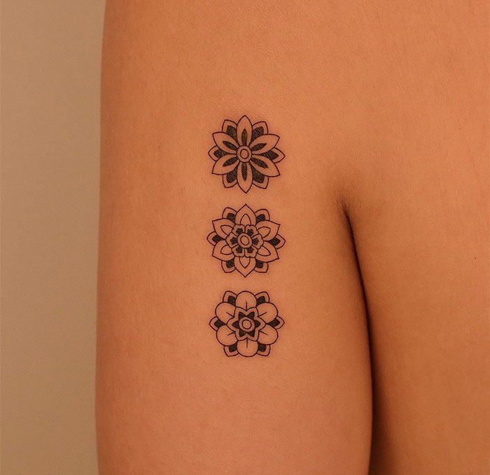 A small tattoo idea featuring three minimalist mandala flowers stacked vertically on the upper arm, each with unique petal designs.