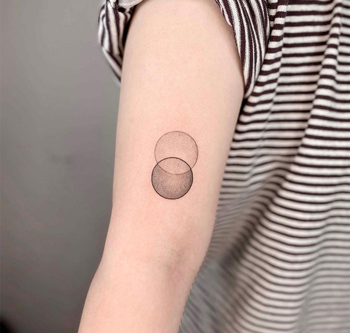 A small tattoo idea featuring two overlapping circles on the arm, creating a minimalist Venn diagram effect.