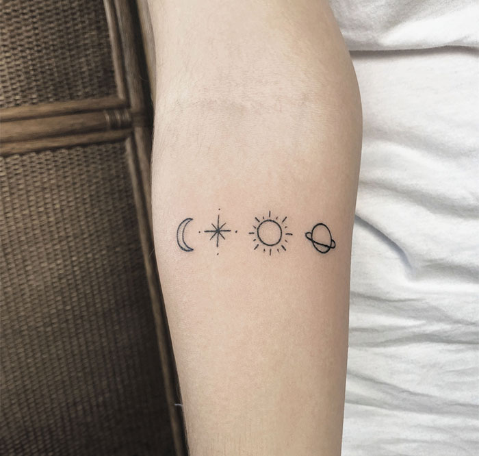 A small tattoo idea featuring celestial symbols—crescent moon, star, sun, and planet—aligned in a simple, minimalist row on the forearm.