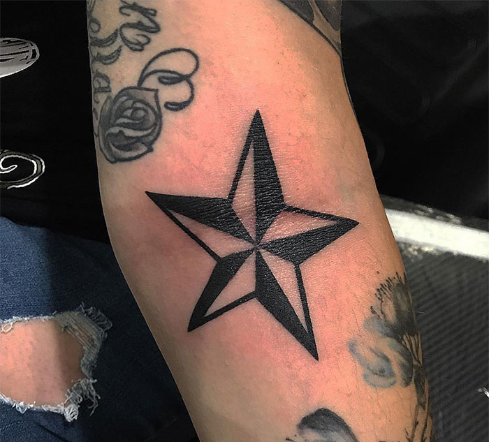 A small tattoo idea featuring a bold black star with angular, intersecting lines on the arm, creating a striking geometric design with a shaded effect.