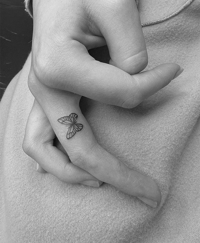 A small tattoo idea featuring a finely detailed butterfly on the side of a finger, adding a subtle, elegant touch to hand art.