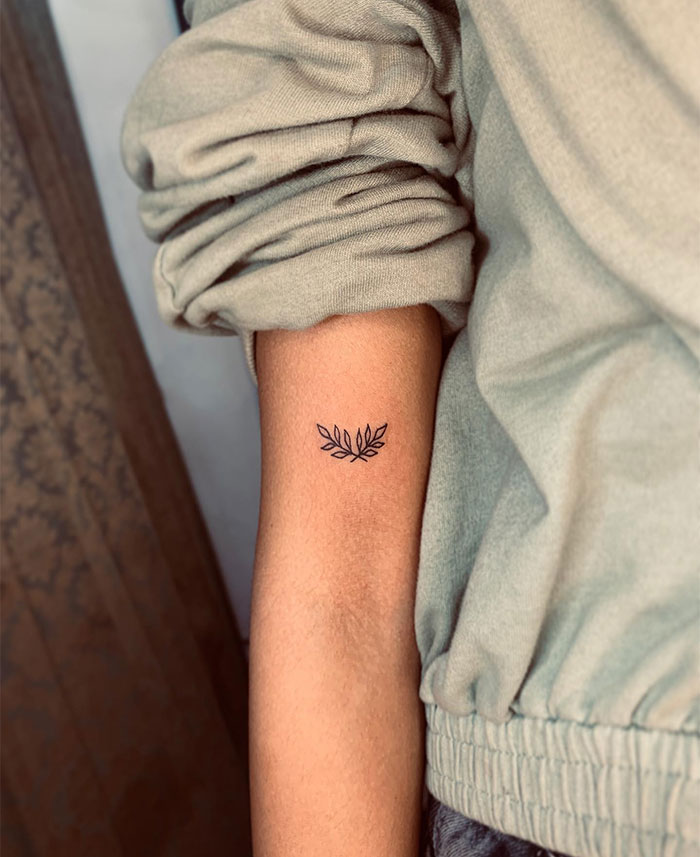 A small tattoo idea featuring a delicate olive branch on the inner arm, symbolizing peace and resilience in a minimalist design.