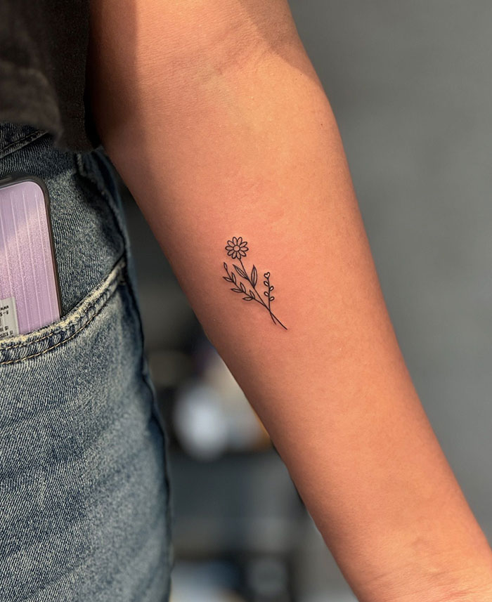 "A small tattoo idea featuring a simple line-drawn flower with leaves on the forearm, adding a delicate and natural touch."