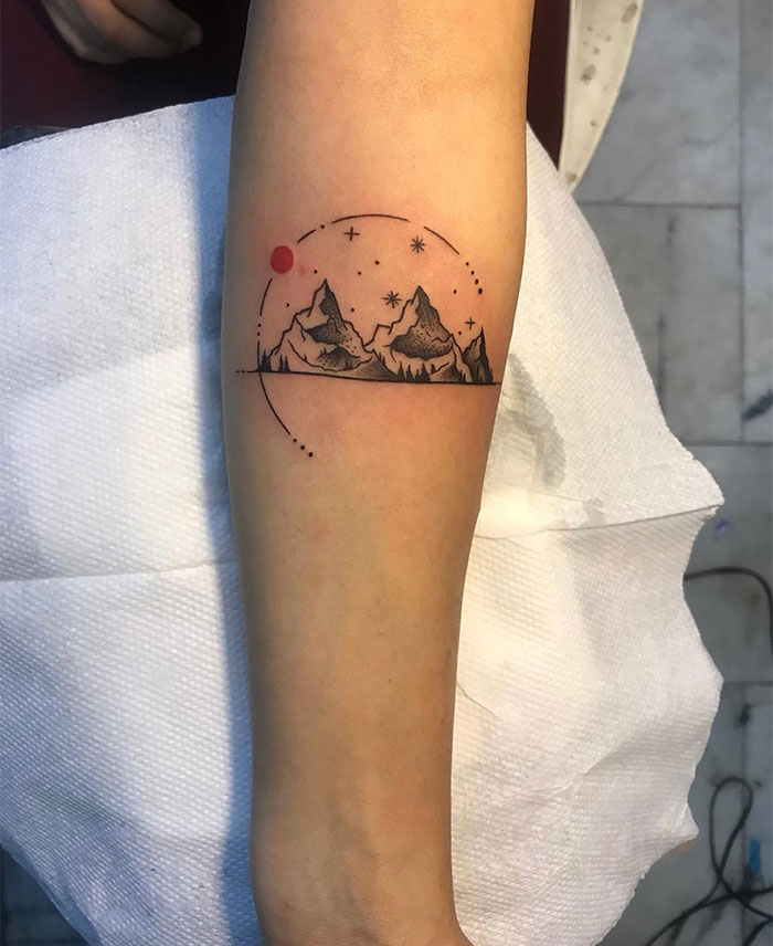 A small tattoo idea featuring a minimalist mountain landscape encircled by stars and a red sun, symbolizing adventure, serenity, and connection with nature.